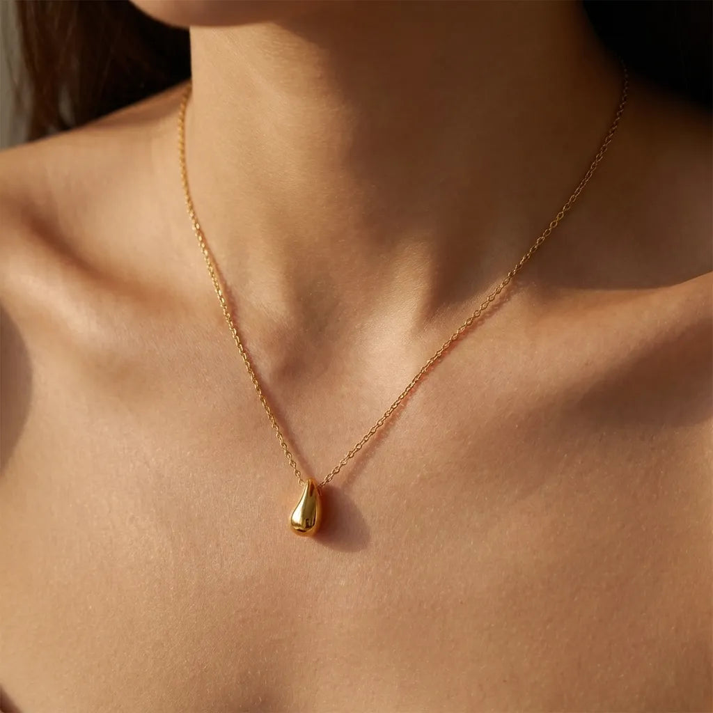 Woman wearing the Sandra necklace, a small polished gold teardrop pendant below the collarbone