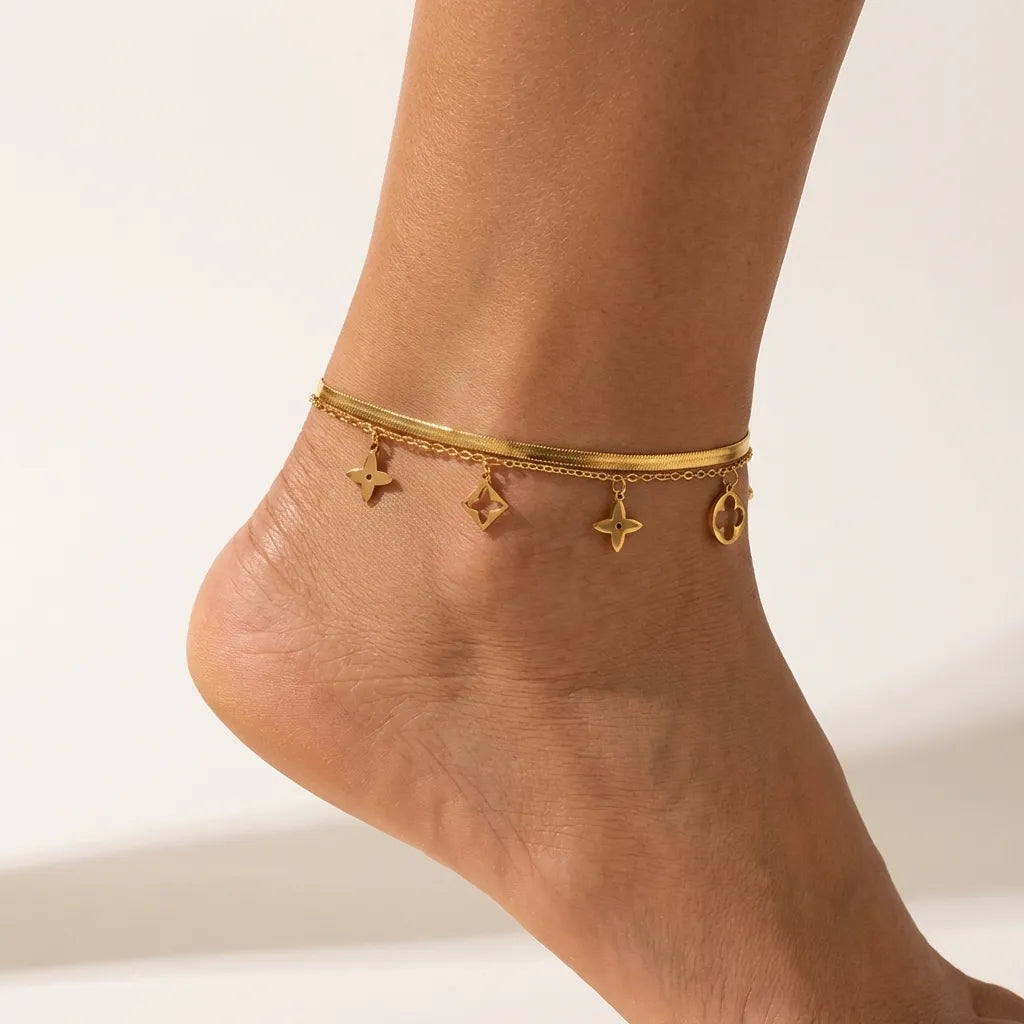Aurélie clover charm anklet on the ankle, cut-out star and clover charms hanging below a flat gold chain