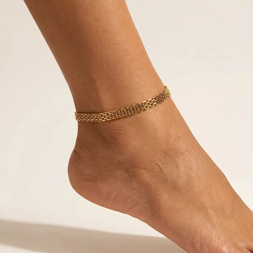 Imara gold chain anklet worn on the ankle, a wide woven band of small rectangular links