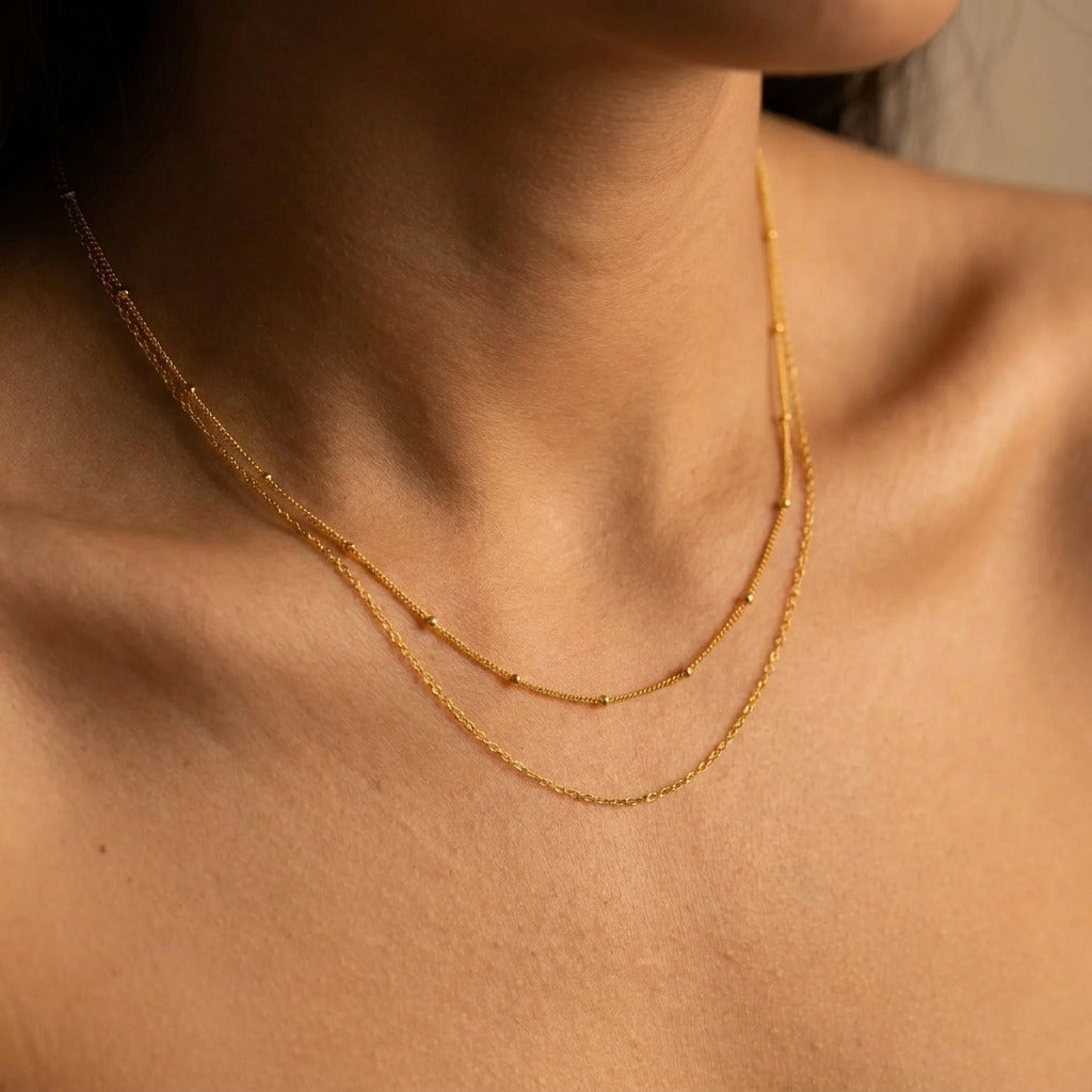 Woman wearing the Ava layered chain necklace in gold, a beaded satellite chain above a finer strand