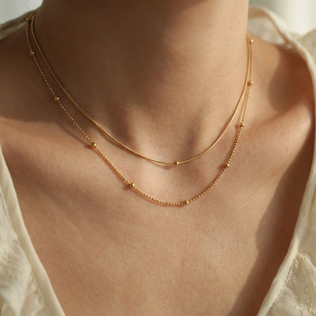 Woman wearing the Mila layered chain necklace in gold, snake chain at the throat over a bead chain