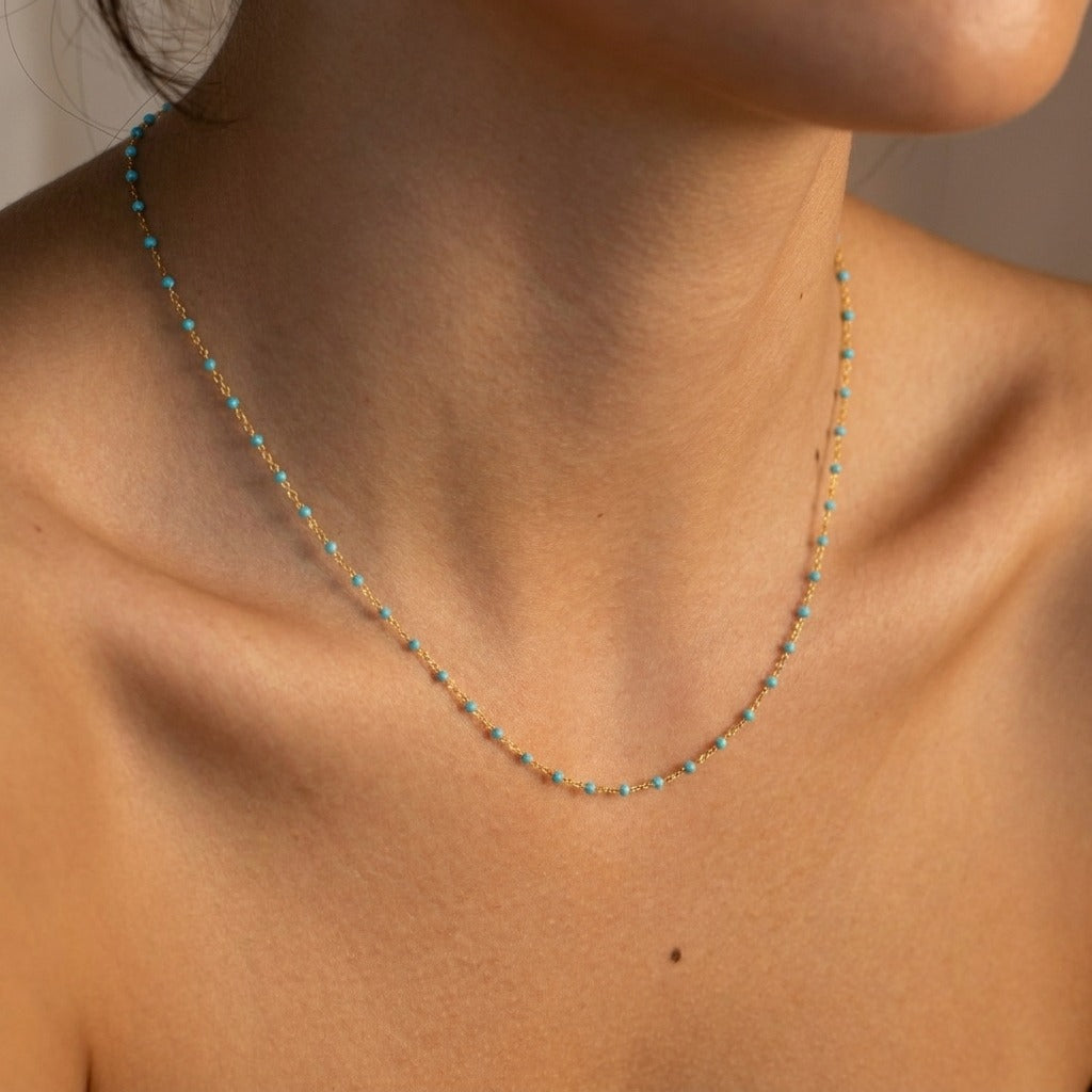 Woman wearing the Capri gold chain necklace dotted with tiny turquoise-blue beads