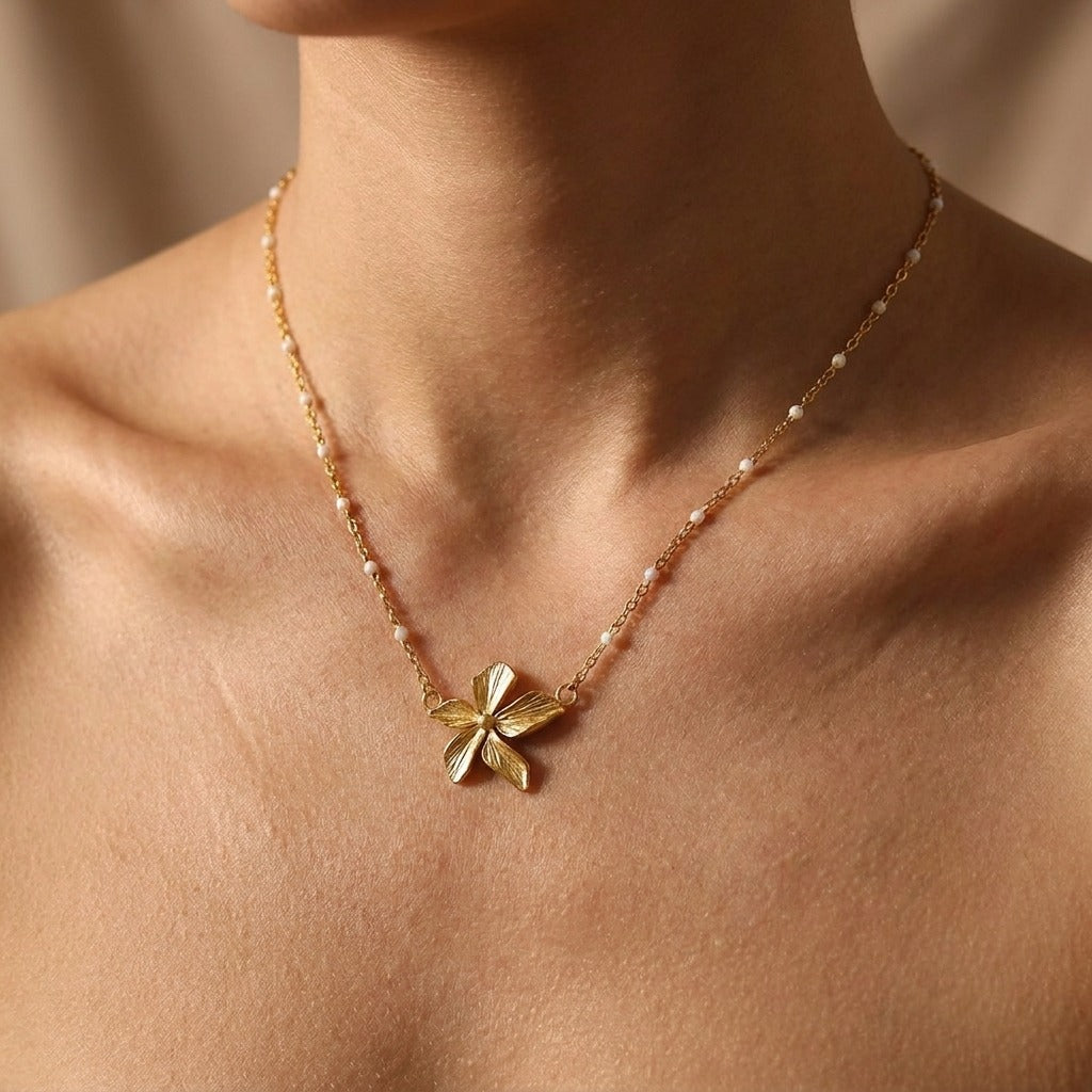 Woman wearing the Flora gold flower necklace on a chain dotted with small white beads
