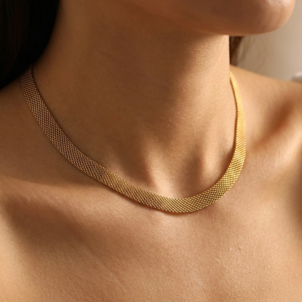 Woman wearing the Élise wide gold mesh necklace lying flat along the collarbone