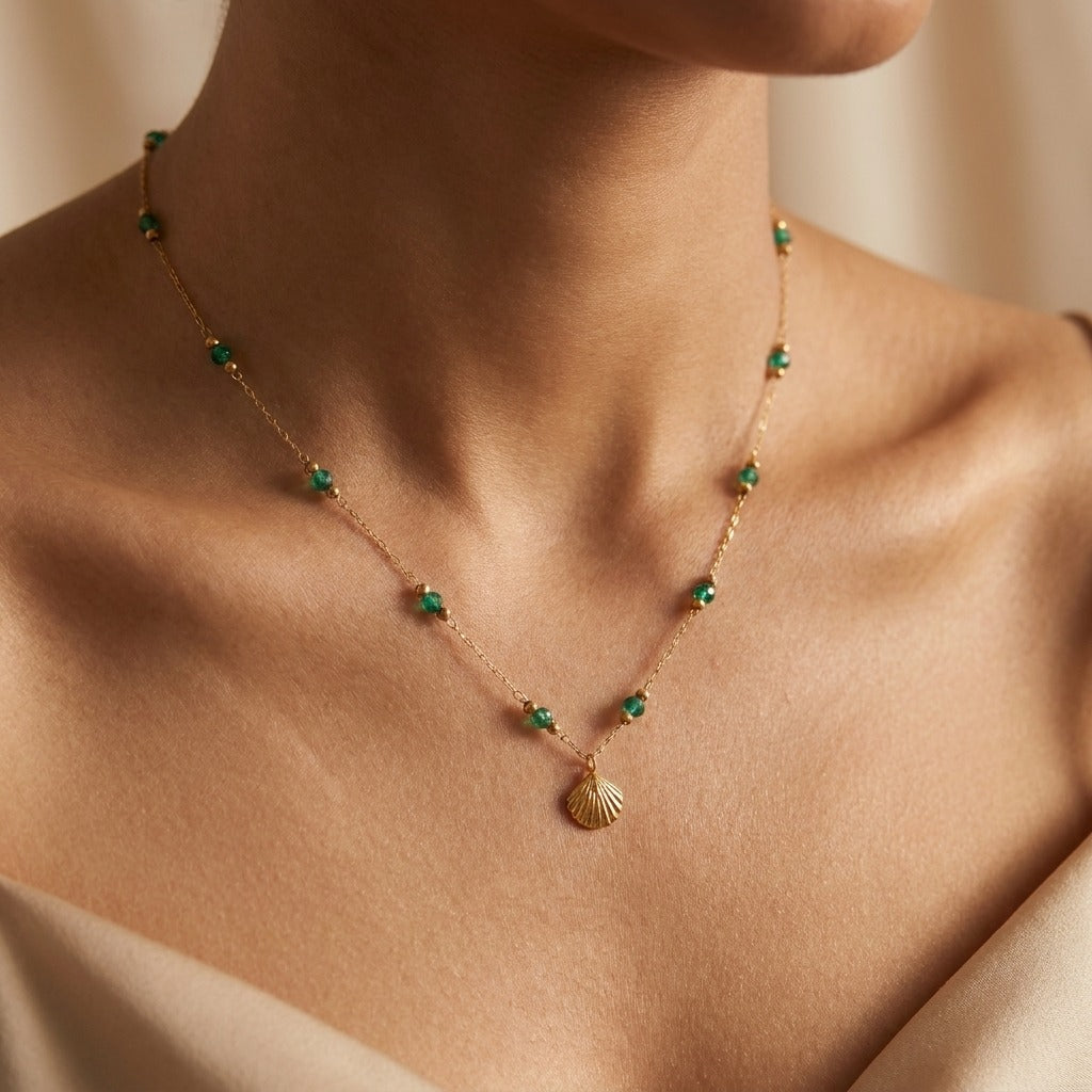 Woman wearing the Alla gold shell necklace with green beads spaced along the chain
