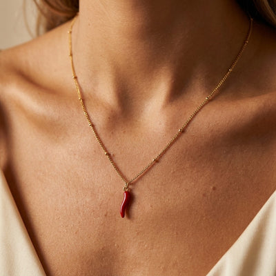 Woman wearing the Chilliana necklace, a red enamel chili charm on a gold satellite chain at the collarbone