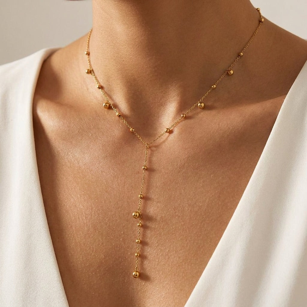 Woman wearing the Aurélie gold Y-shaped necklace with gold beads dropping down the neckline