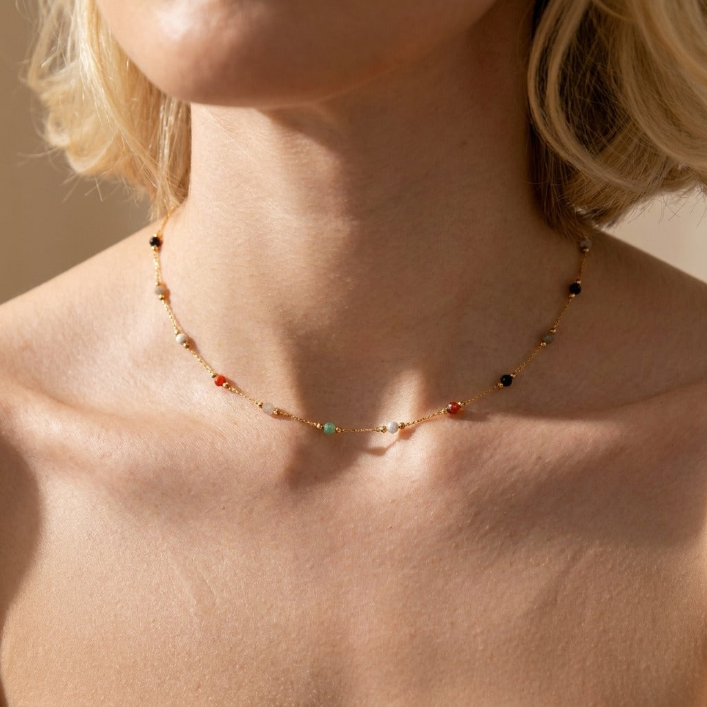 Woman wearing the Alla gold chain necklace with small black, red, green and white stone beads