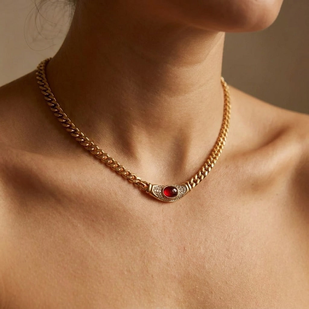 Woman wearing the Vintage Isabella gold curb chain necklace with a red oval stone at the base of the neck