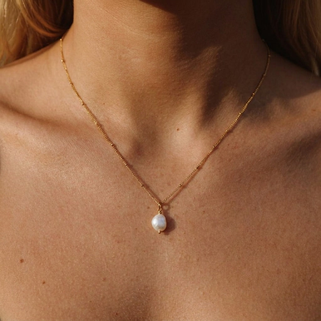 Woman wearing the Luna pearl pendant in gold, a baroque pearl at the collarbone in sunlight