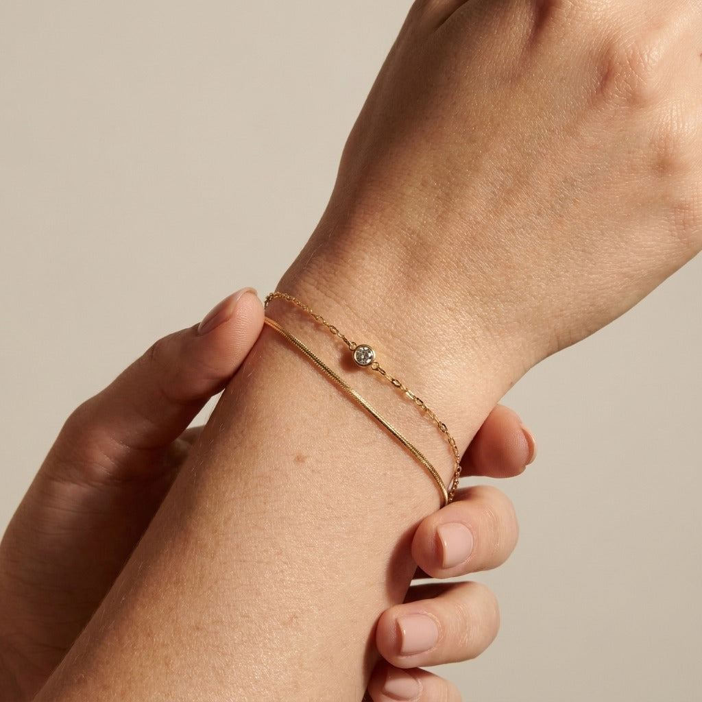 Amélie double-chain bracelet in gold on the wrist, a snake chain beside a fine chain with one crystal