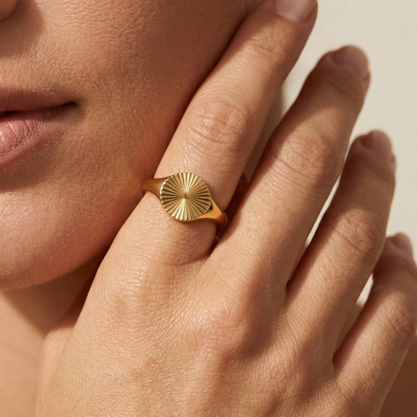 Solana gold signet ring with a fluted sunburst face, worn on a hand resting at the cheek