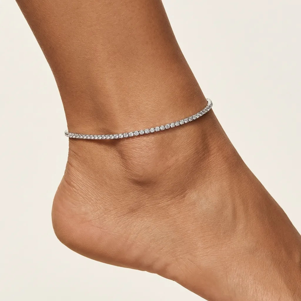 Woman wearing the Sophie Lumière tennis anklet in silver, a fine unbroken row of crystals on the ankle