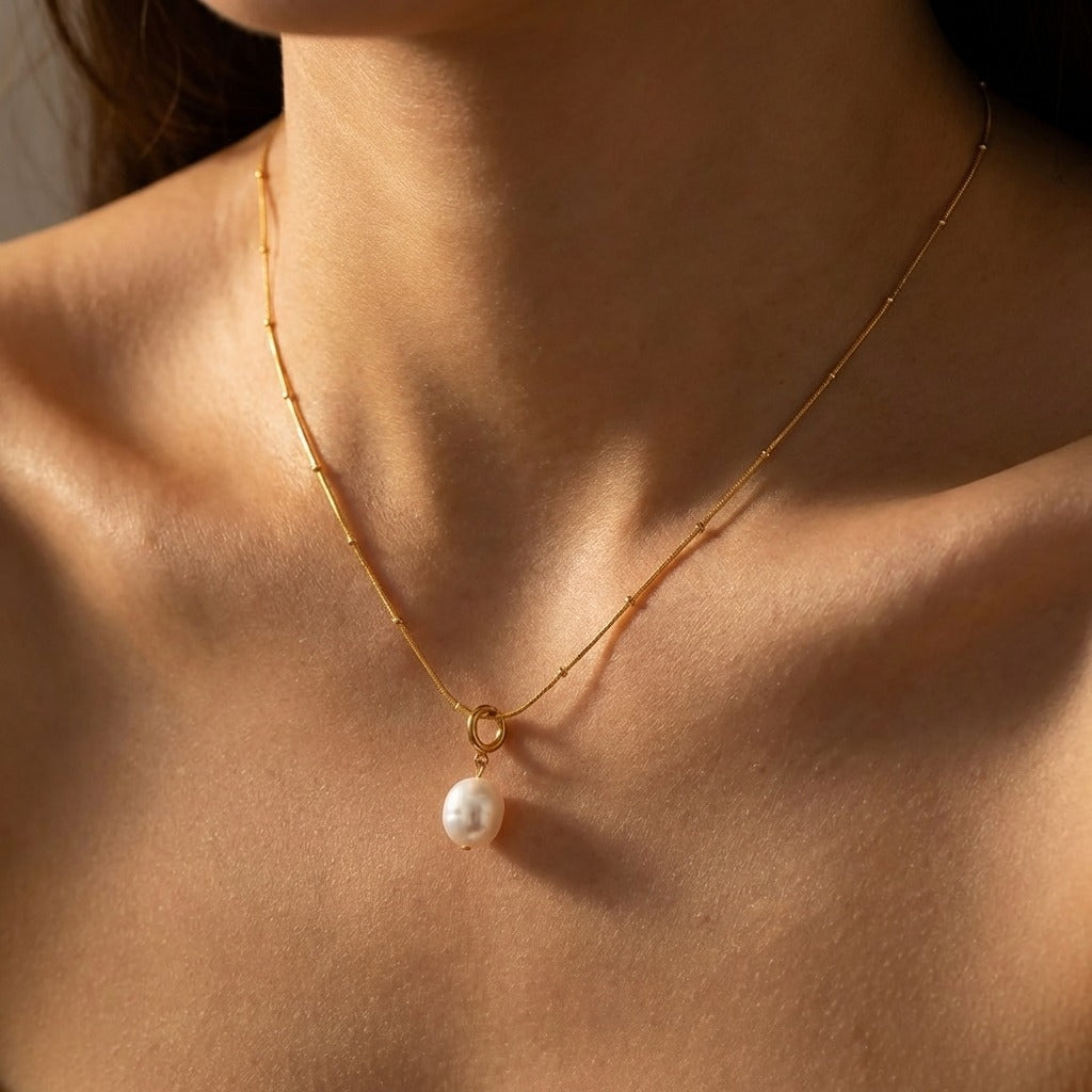Woman wearing the Léa oval pearl charm necklace, oval pearl hanging from a gold ring