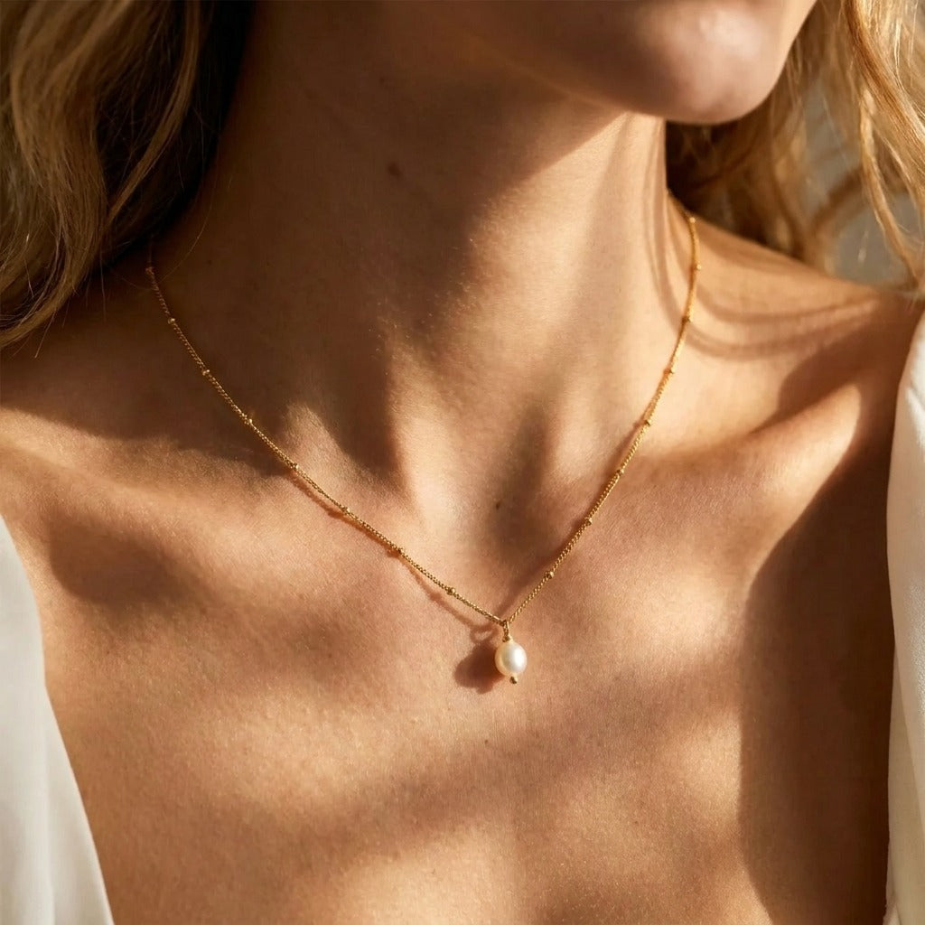 Woman wearing the Léa dainty pearl drop necklace in gold, one pearl on a satellite chain