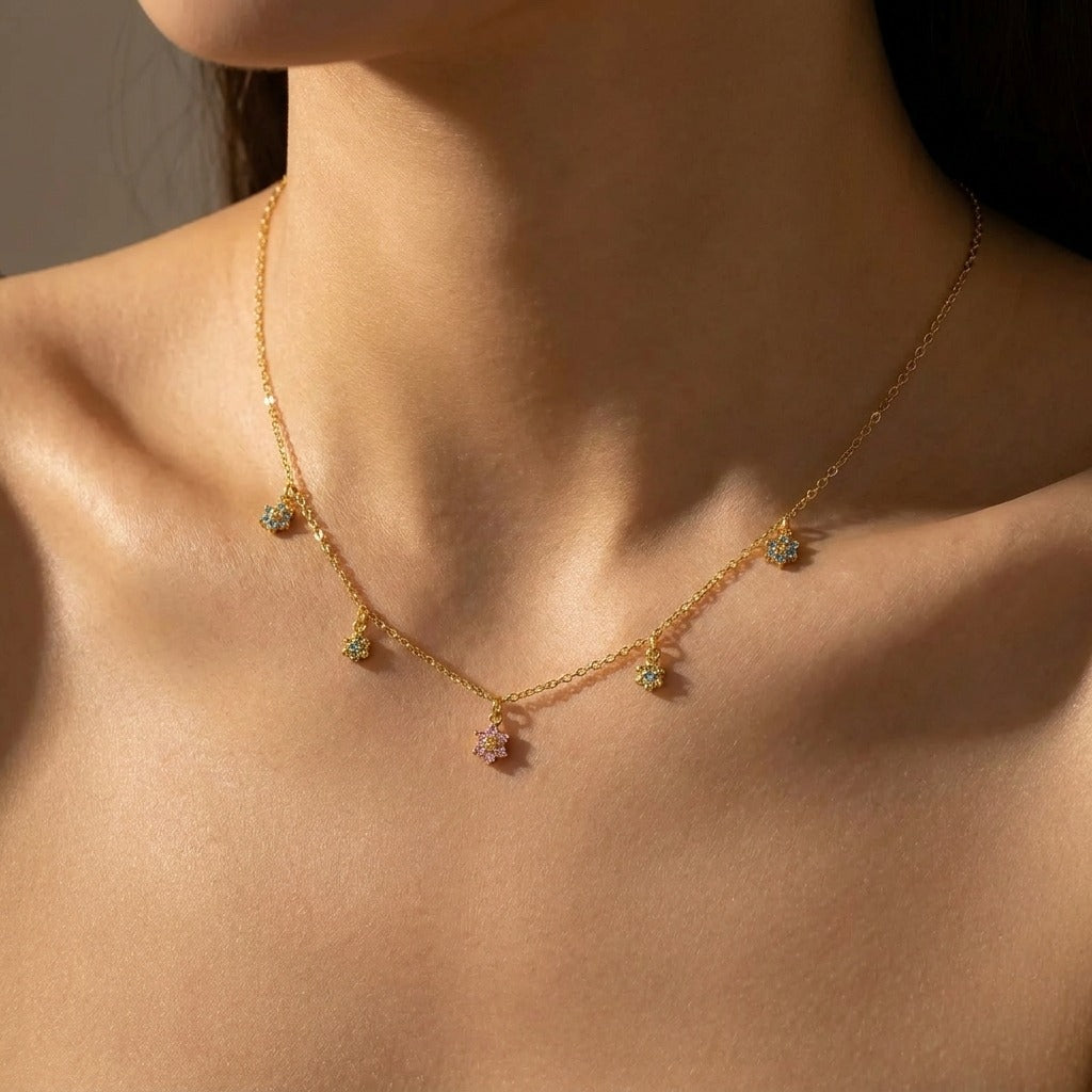 Woman wearing the Sofia blossom charm necklace in gold with pink and blue-green crystal flowers