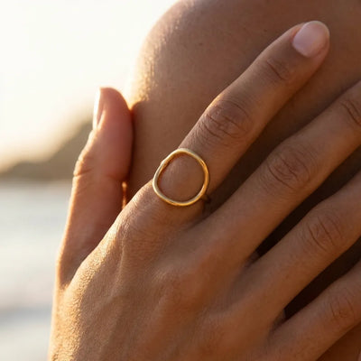 Woman's hand wearing the Alice open oval gold ring, lit by a low sunset