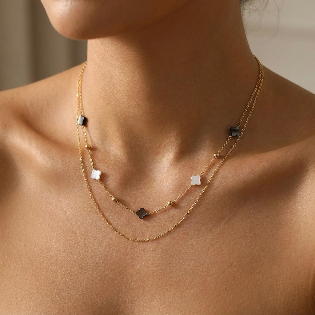 Woman wearing the Elodie shell clover necklace in gold, white and dark clovers layered over a fine chain