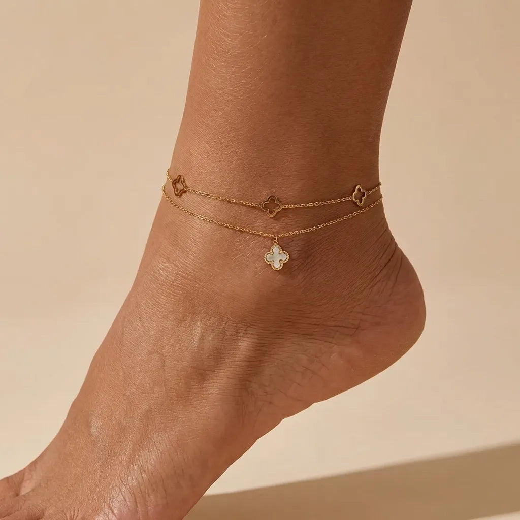 Woman wearing the Rowena clover gold anklet, open clover links above a white clover charm on the ankle