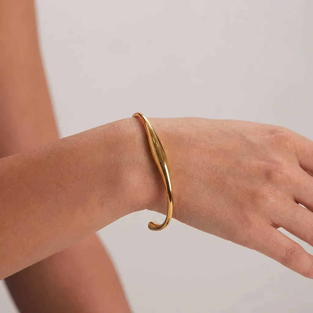 Woman wearing the Tiffany gold bangle, an open cuff with a fluid sculpted curve, on the wrist