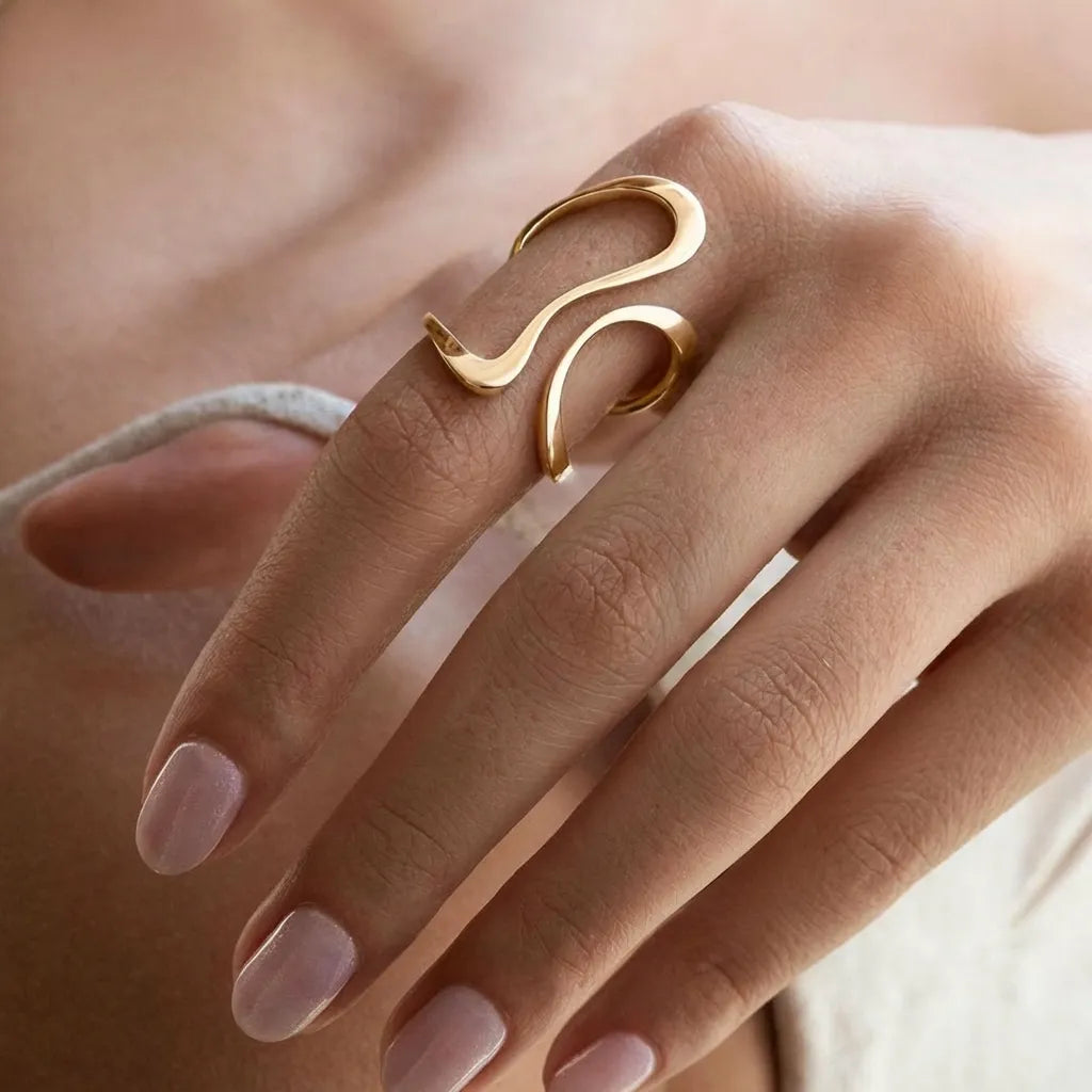 Hand wearing the Mosaic gold ring, a slim polished wave curving up the finger