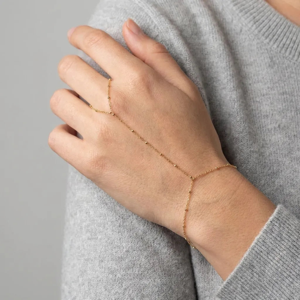 Woman wearing the Evelyne gold hand chain across the back of her hand, looped around one finger