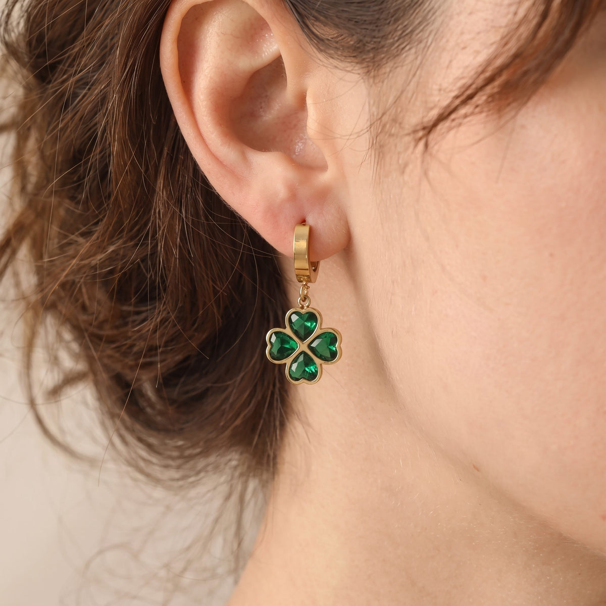 Woman wearing the gold clover earrings, heart-shaped green crystal leaves hanging from a small huggie