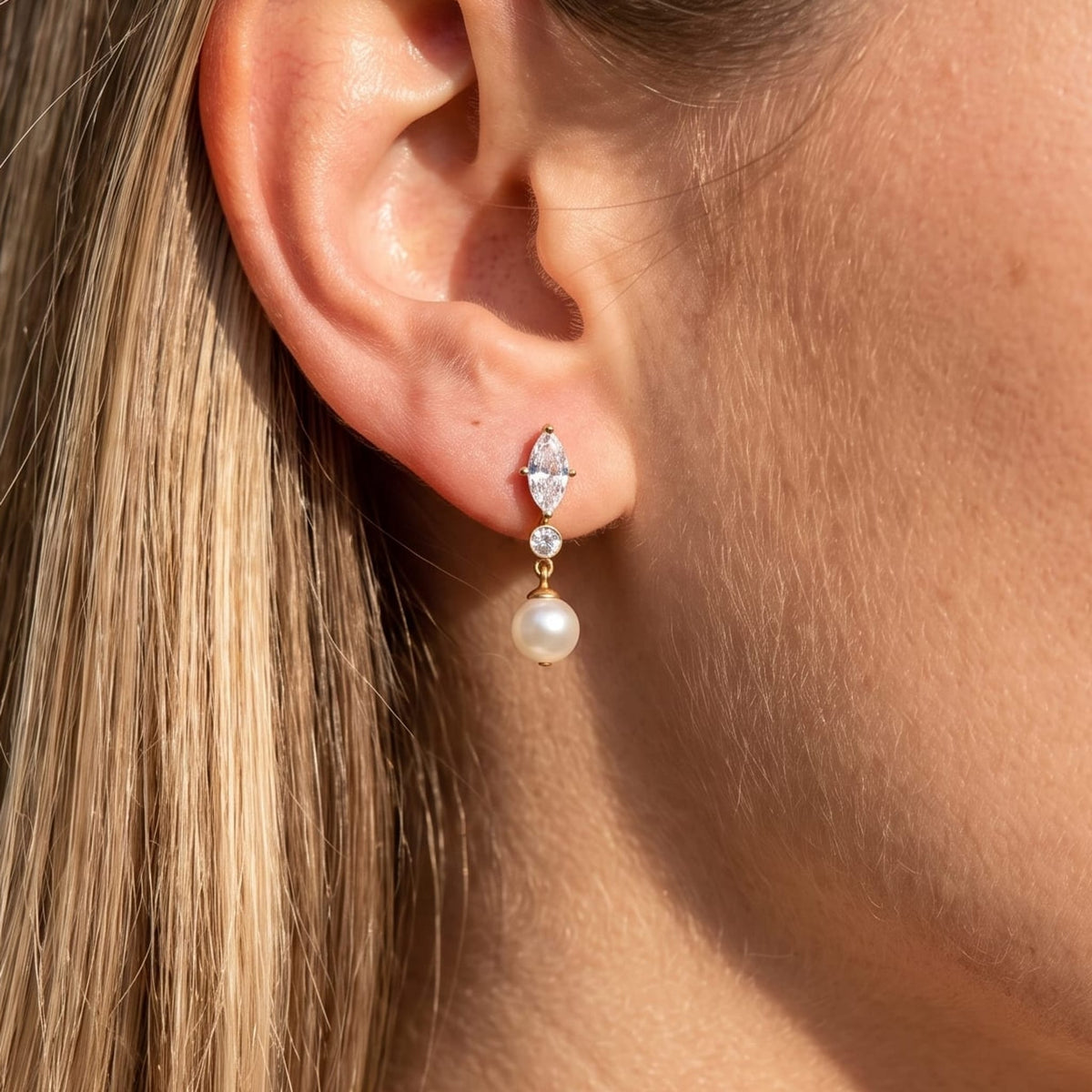 Woman wearing the Emilia marquise pearl gold earrings on her ear close up in sunlight
