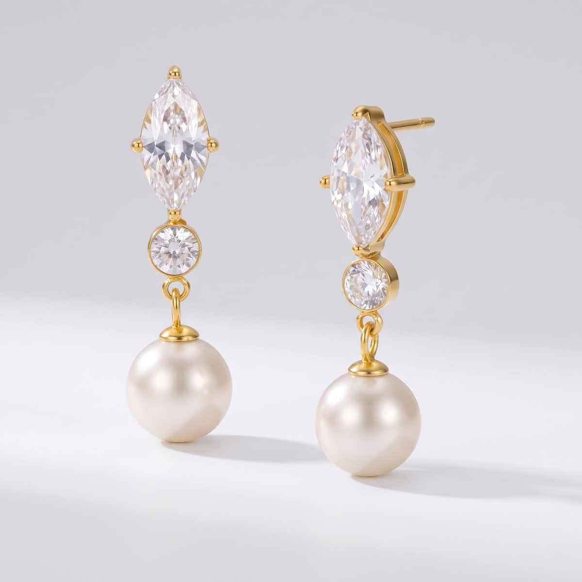 Emilia marquise pearl gold earrings on a plain white surface casting soft shadows