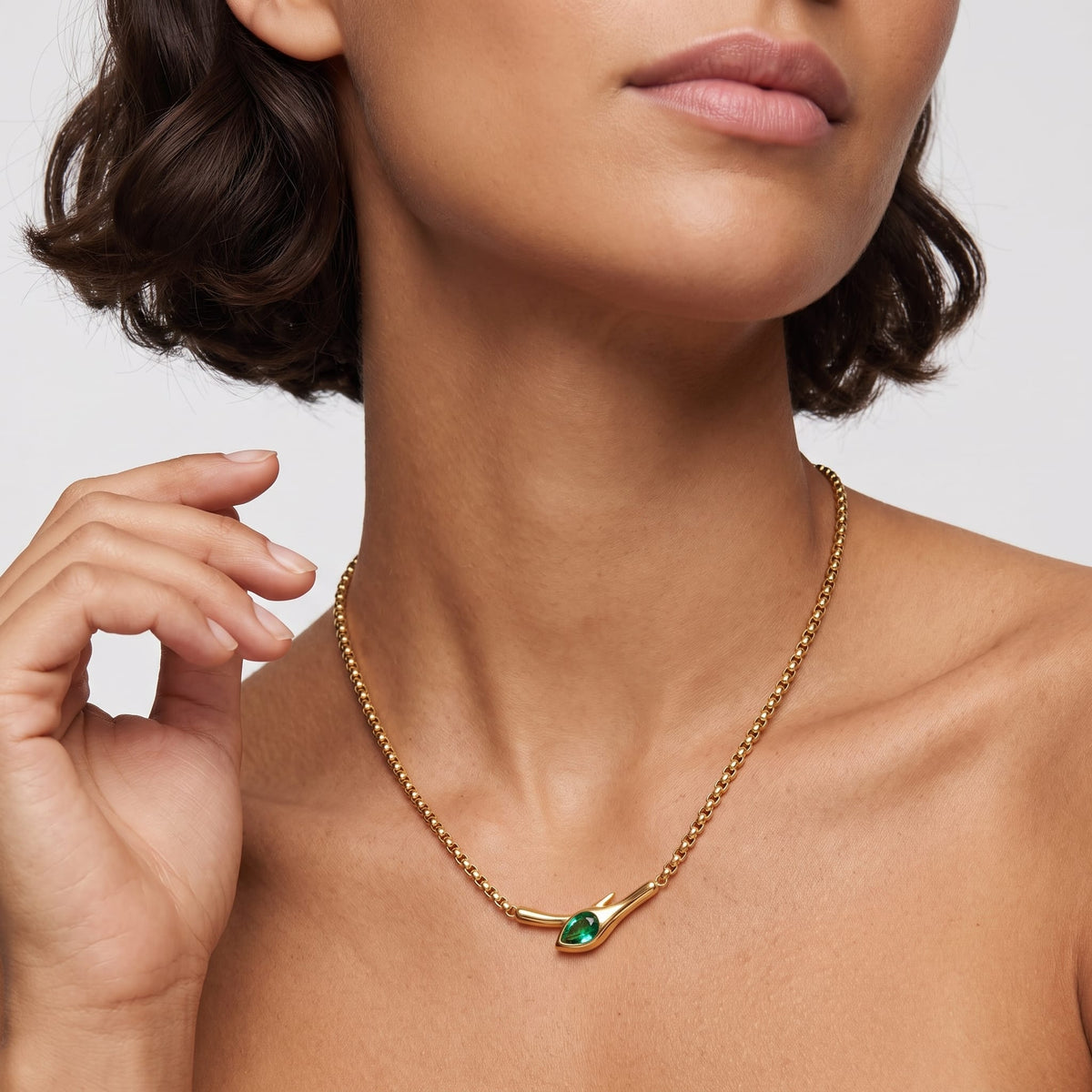 Woman wearing the Gemma green snake gold necklace at the collarbone resting her hand near her hair