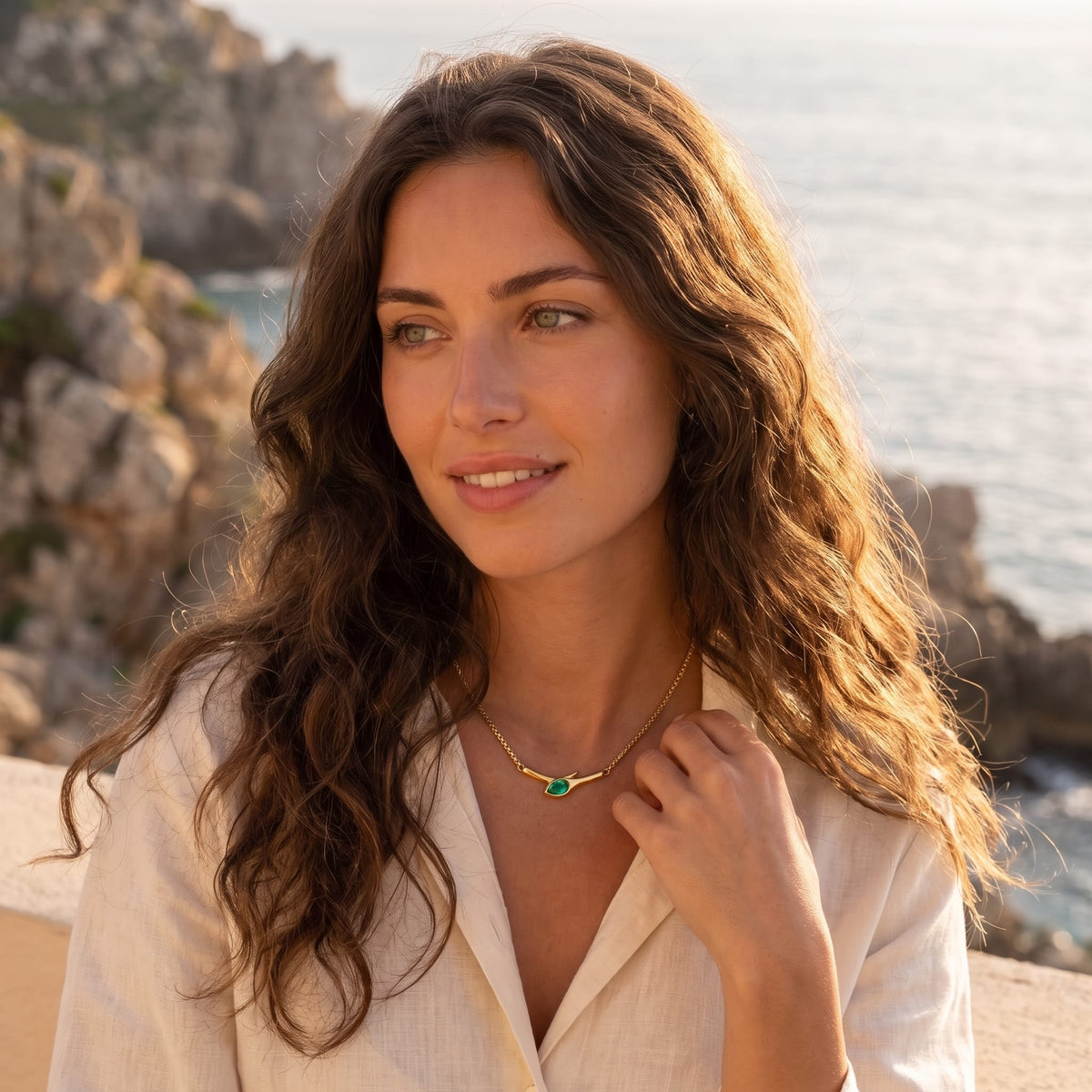 Woman wearing the Gemma green snake gold necklace at the collarbone outdoors in a white linen shirt