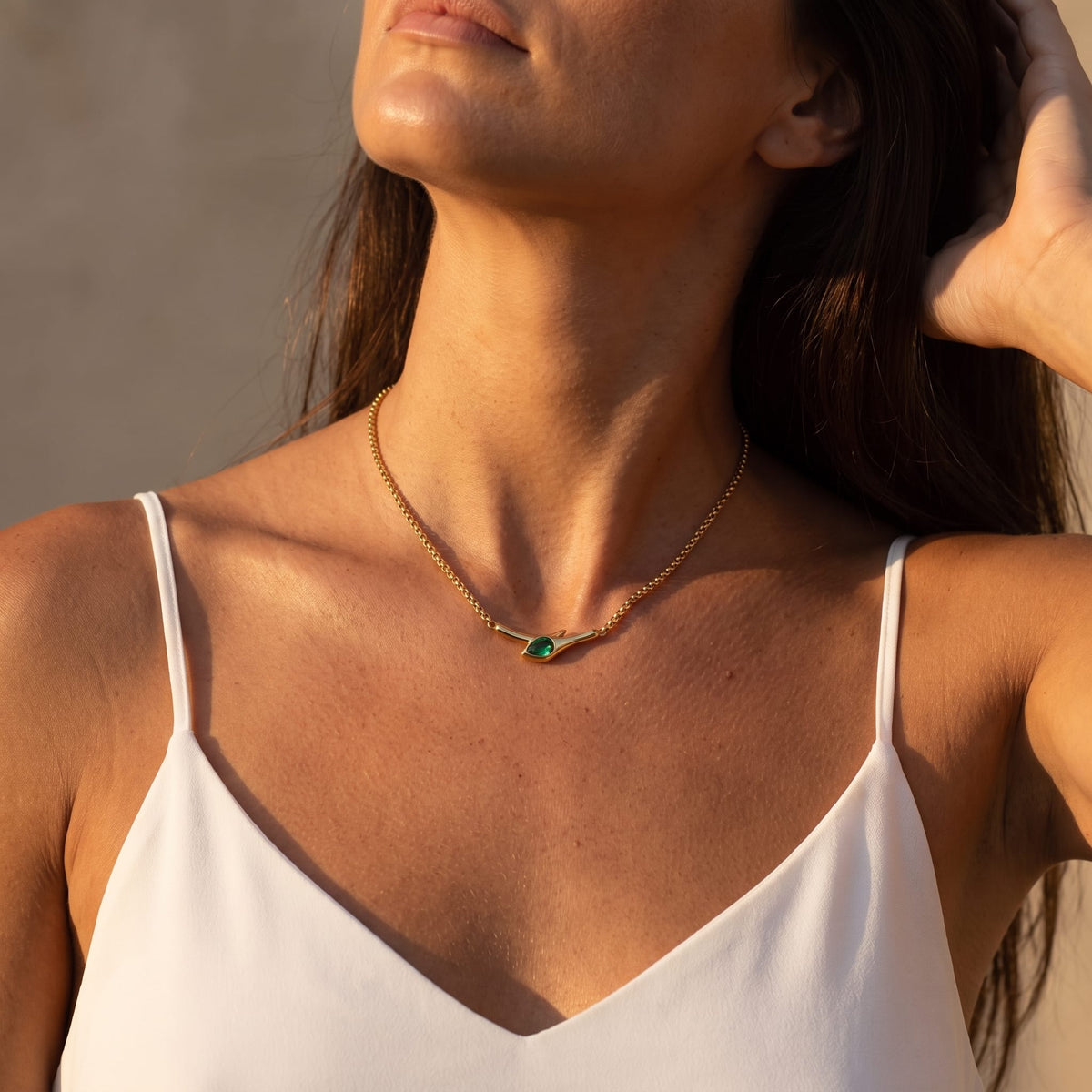 Woman wearing the Gemma green snake gold necklace at the collarbone wearing a white strap top