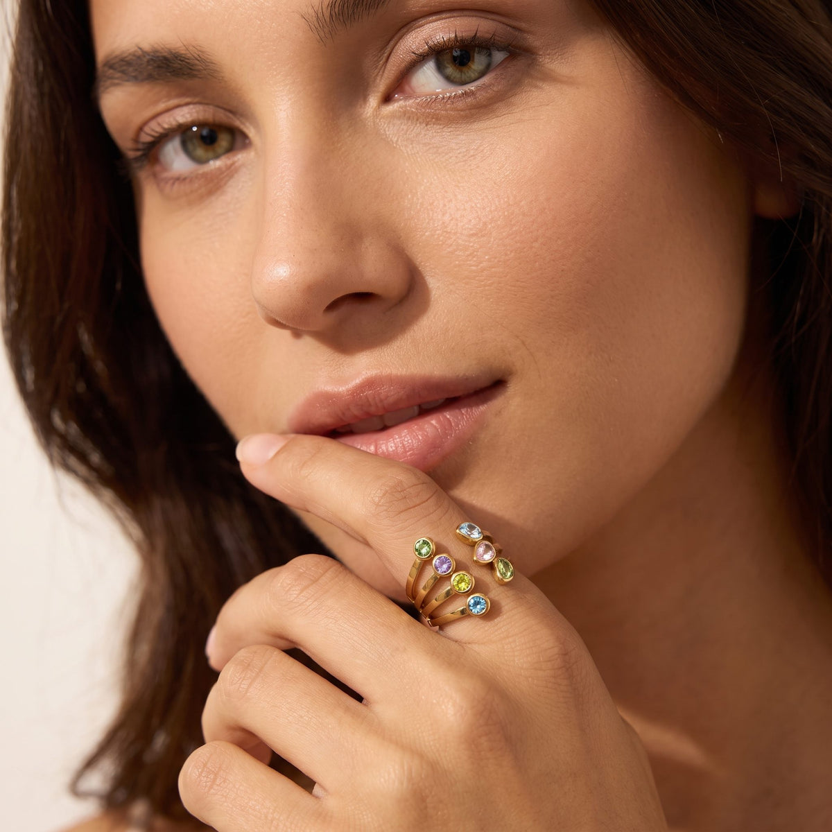 Woman with a fingertip at her lip, wearing the Giulia pastel crystal gold ring