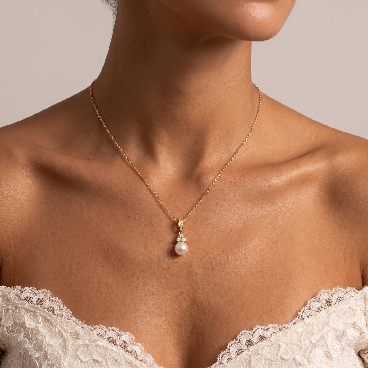 Wider view of a woman wearing the Hortense pearl pendant gold necklace at the collarbone paired with a lace dress