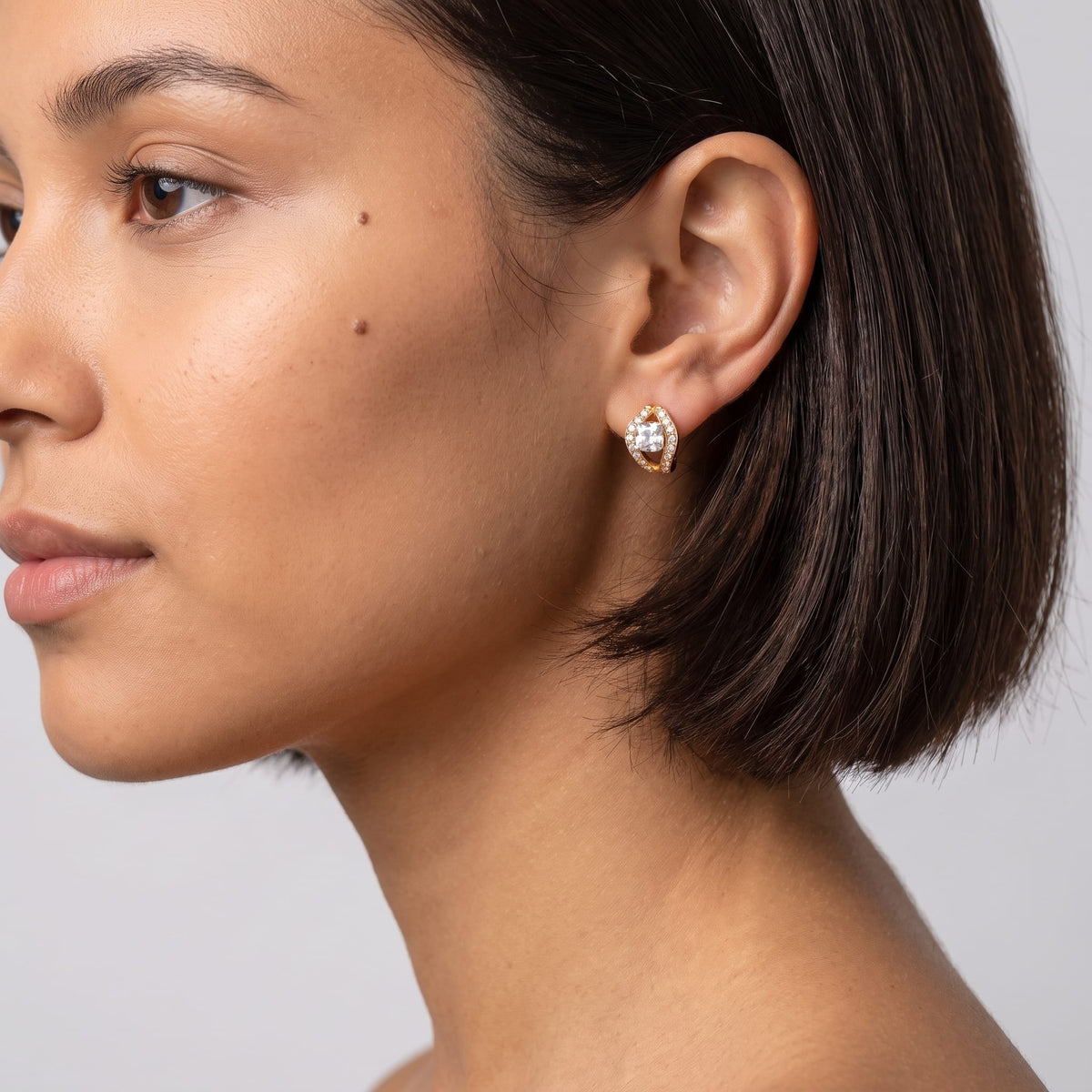 Woman wearing the Ilaria cushion halo gold earrings on the ear with short dark hair in profile