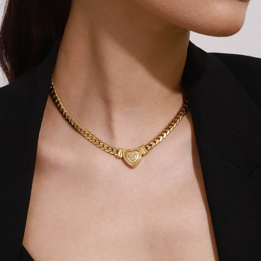 Gold chain necklace with a heart-shaped pendant worn by a person against a neutral background
