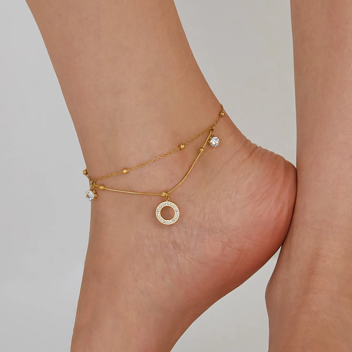 Aurélie circle charm anklet worn on the ankle, a crystal-set open circle and crystal drops on gold chains