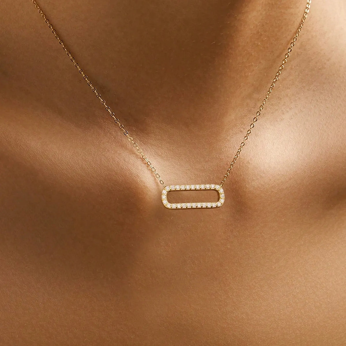 Woman wearing the Elodie oval sparkle necklace in gold, an open crystal-set oval centered below the throat