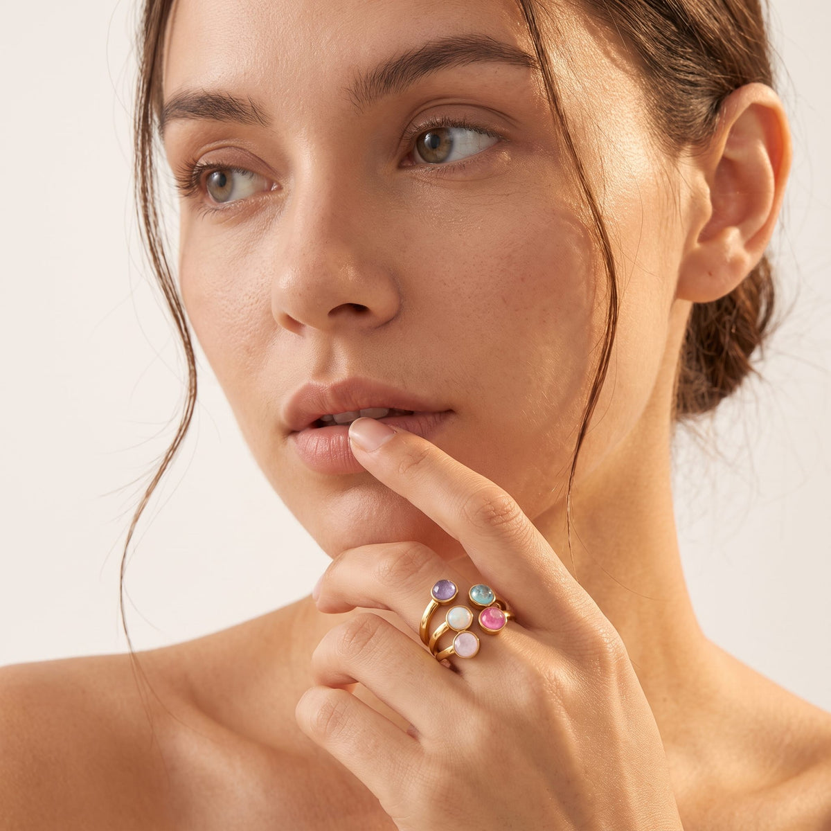 Close-up of a woman's face and hand wearing the Isabella rainbow stone gold ring