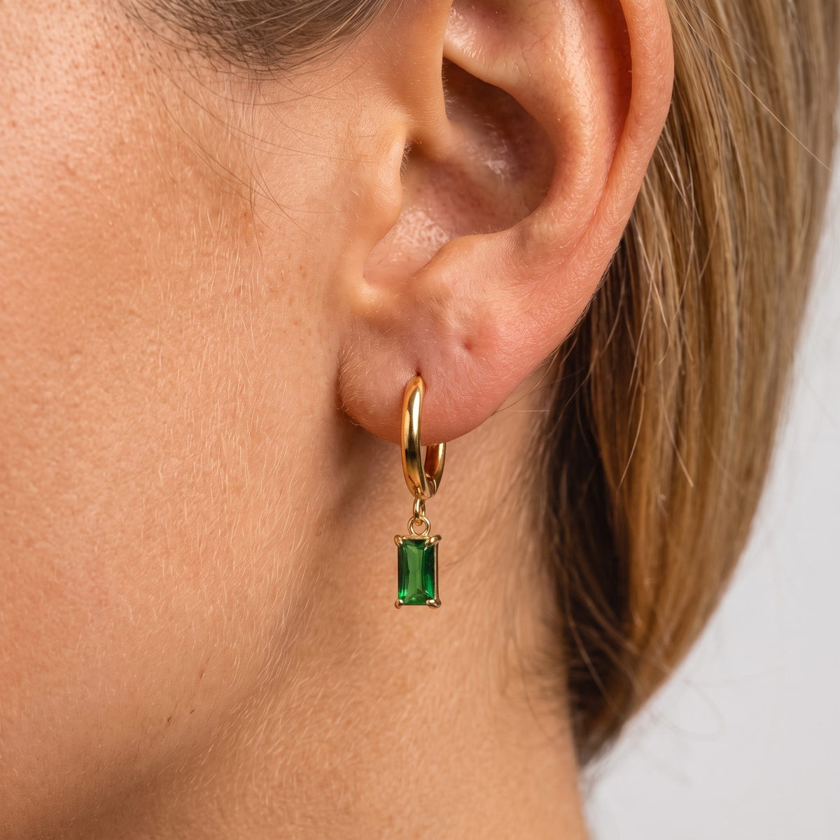 Woman wearing the Jasmine green earring, a rectangular green stone hanging from a gold huggie
