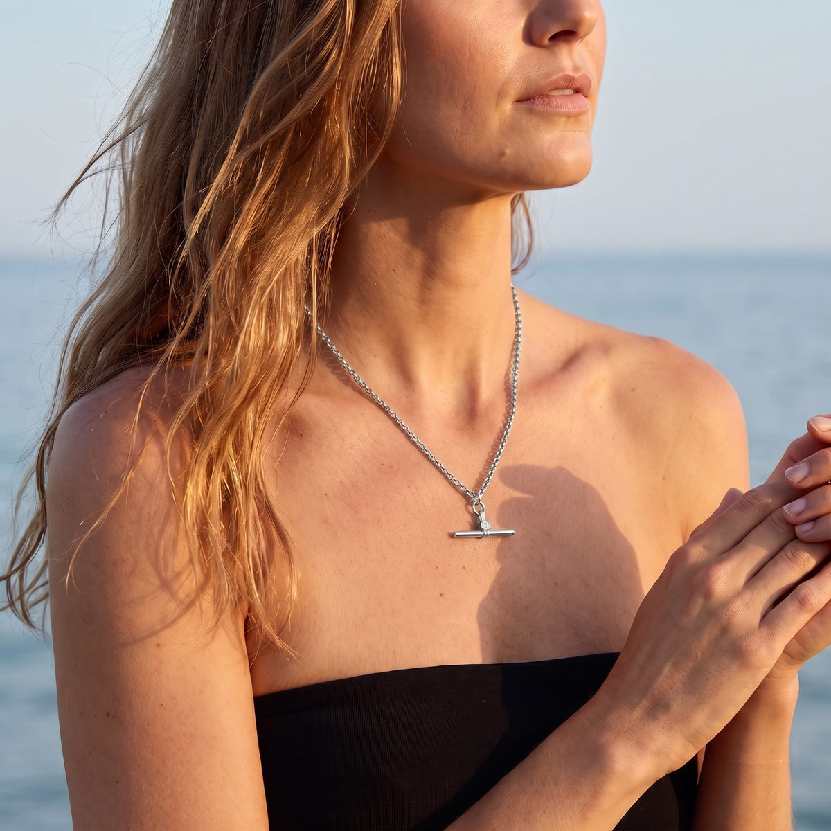 Woman wearing the Joséphine t-bar crystal silver necklace at the collarbone near the ocean