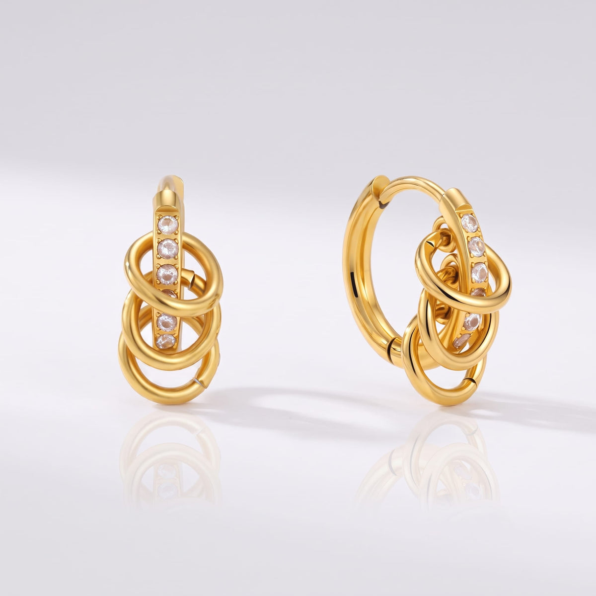 Joséphine triple loop gold earrings on a reflective white surface displaying sparkling stone details