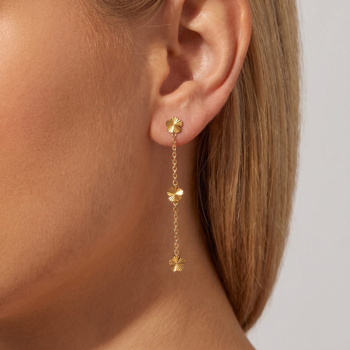 Woman wearing the Juliette gold earring, three small fluted flowers on a fine drop chain