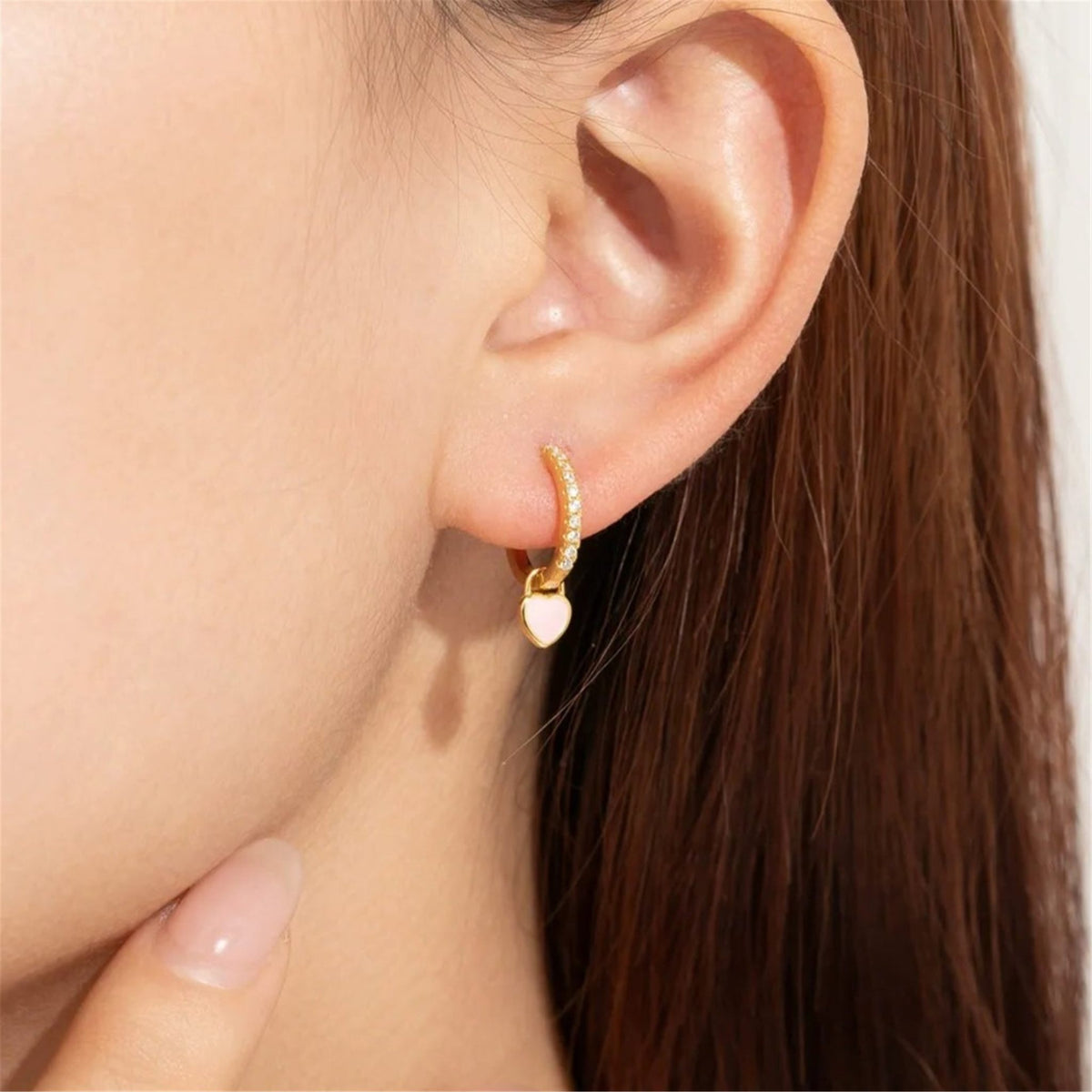 Woman wearing a Juliette gold crystal huggie with a pink heart charm on the ear