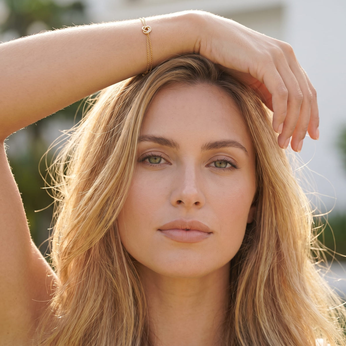 Woman wearing the Juliette love knot gold bracelet on the hand raised near her head outdoors