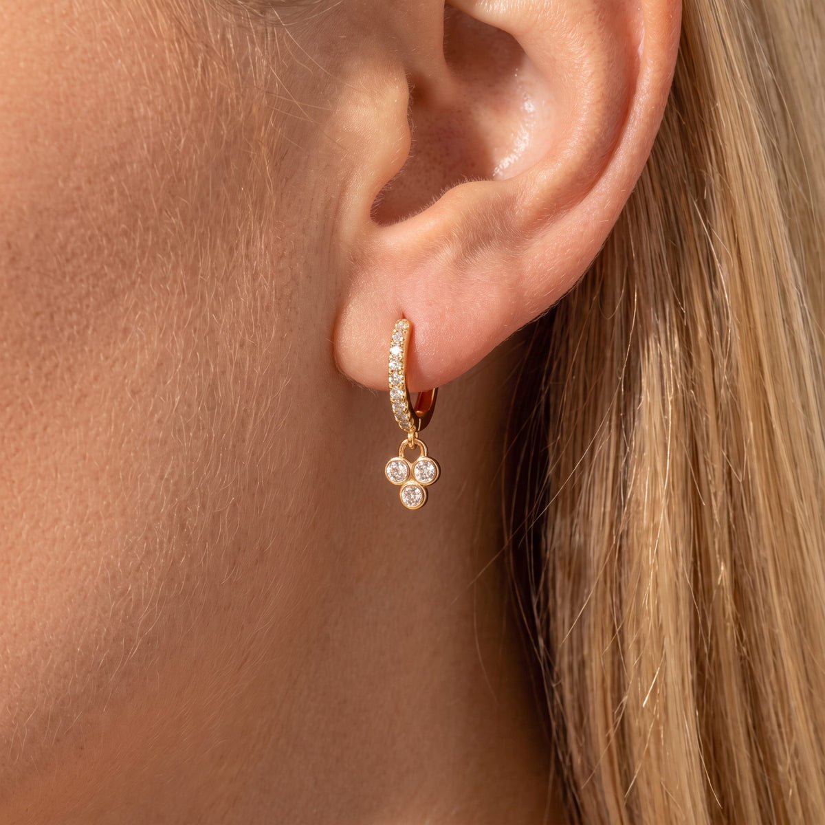 Woman wearing a Juliette gold pavé huggie with a dangling trefoil of round crystals on the ear