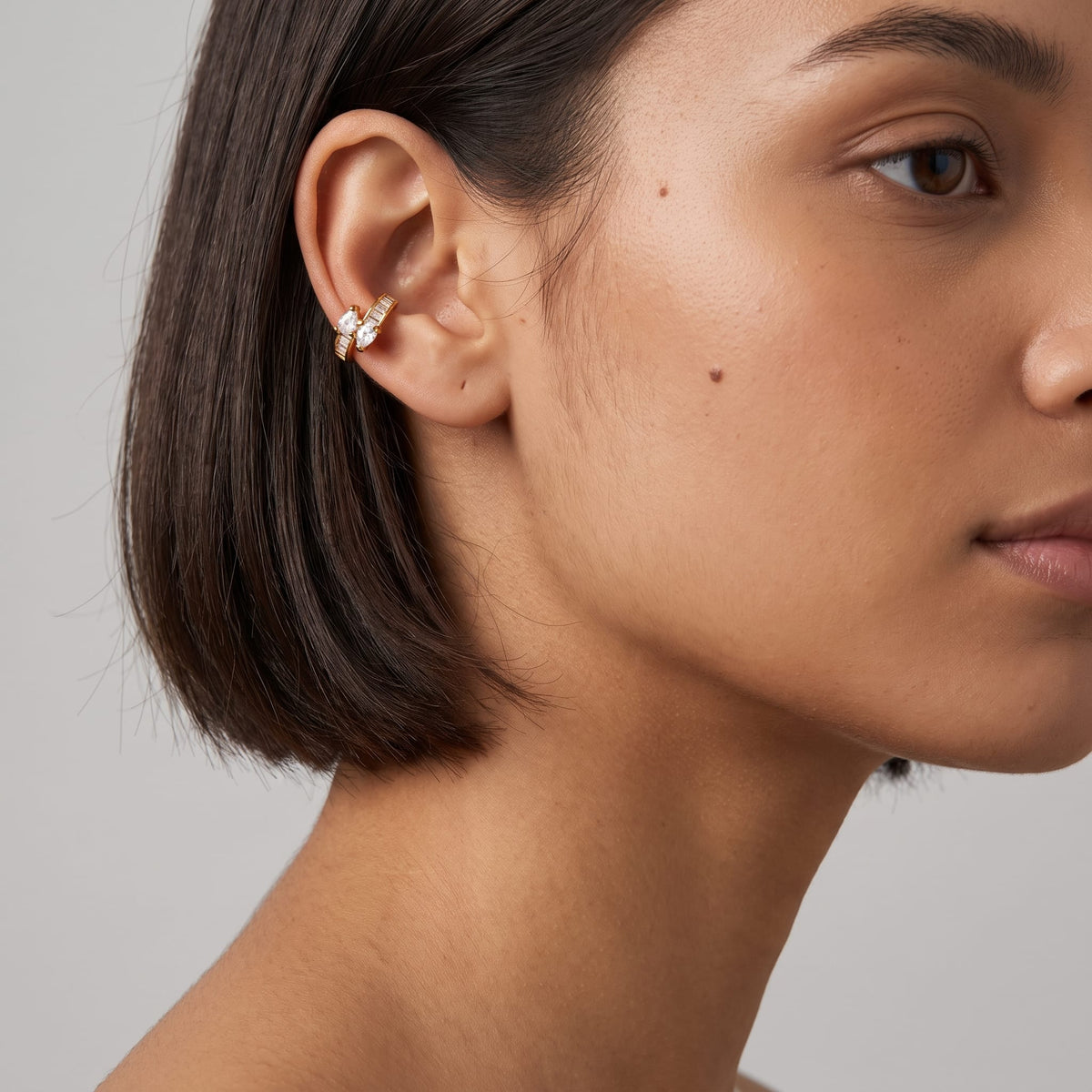 Woman wearing the Laure baguette gold ear cuffs on her ear with dark short hair