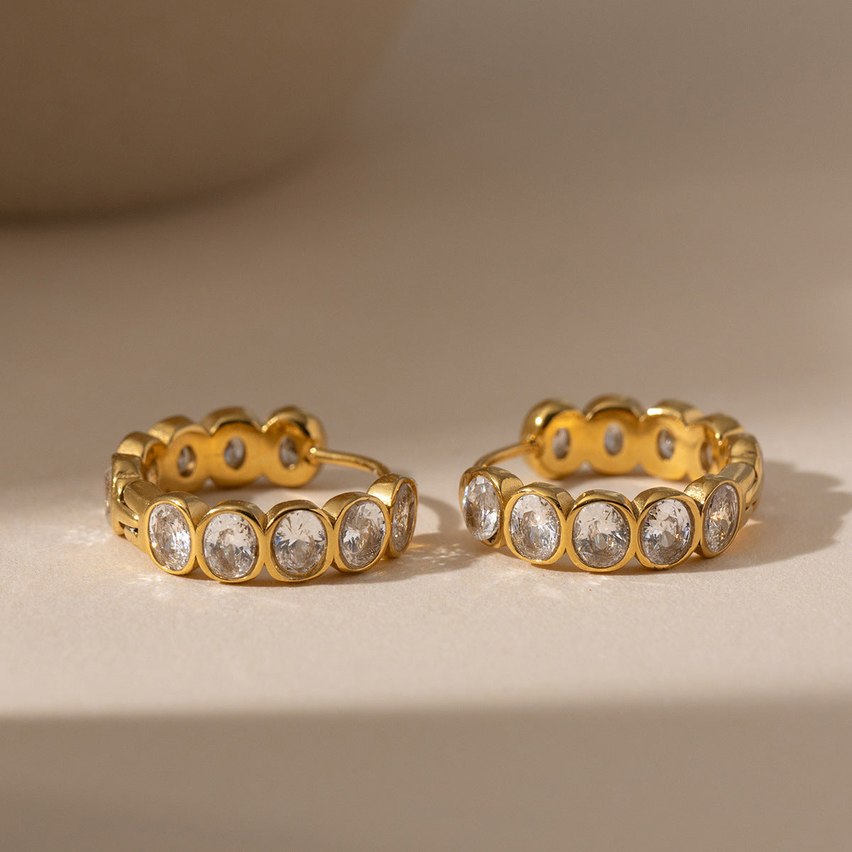 Léa bezel huggie gold earrings resting on a sunlit beige surface