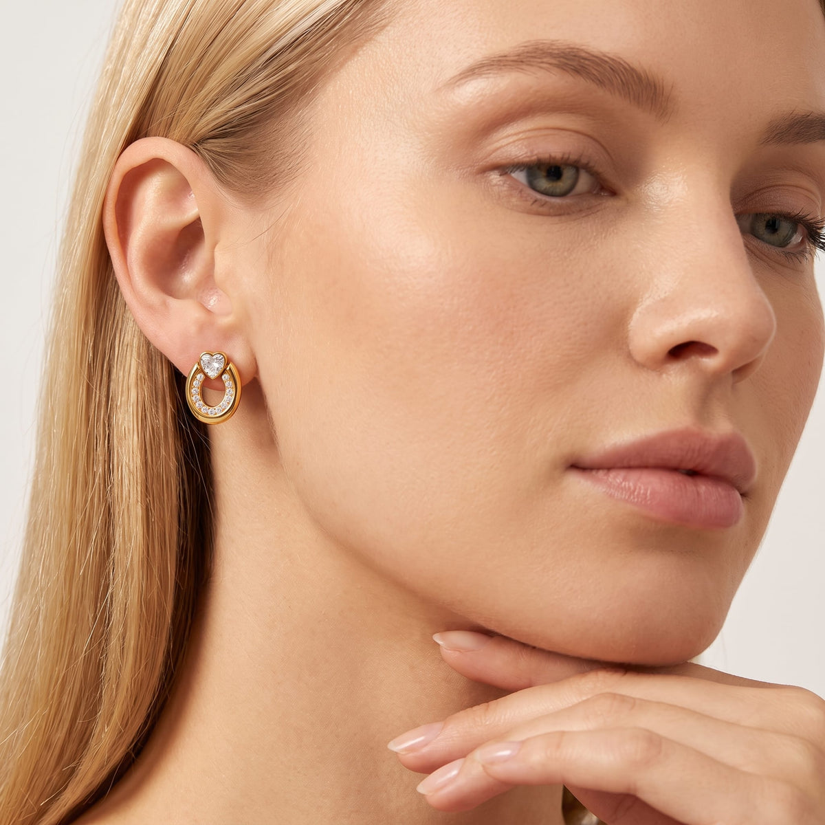 Woman wearing the Léonore horseshoe crystal gold earrings on her ear holding her chin