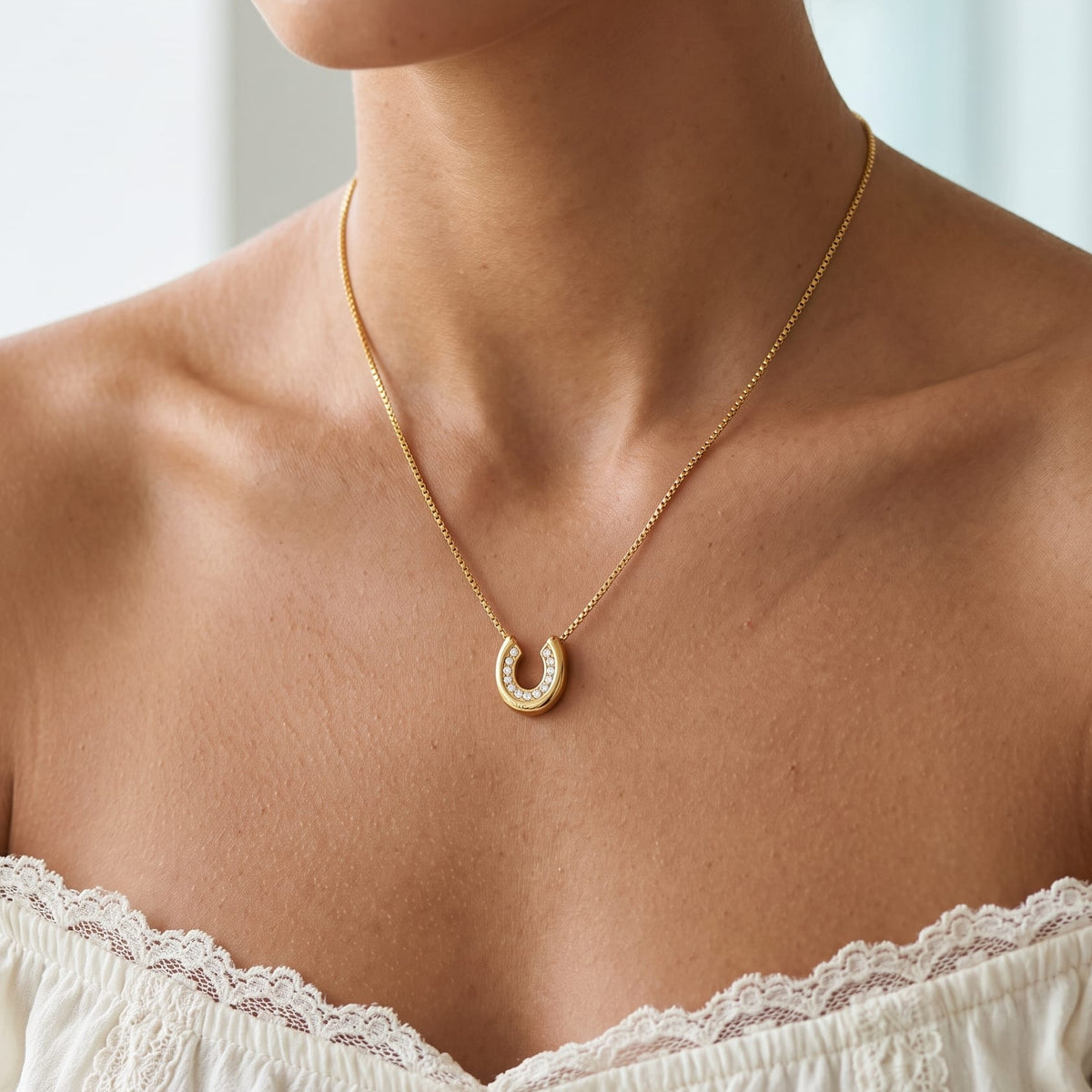 Woman wearing the Léonore horseshoe crystal gold necklace at the collarbone in an off-shoulder lace top